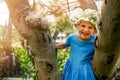 Happy little girl climbs a tree in park on sunny summer day