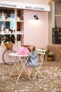 Happy little girl with curly hair in a dress and in a beret sits at a table with a bouquet of pink peonies in a street vintage caf Royalty Free Stock Photo