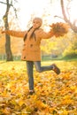 Happy little girl dancing on the fallen maple leaves in autumn park on cheerful fall day, vertica