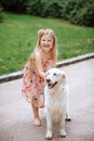 Happy little girl with a dog standing on the road in the park. Cute little girl hugging a dog, smiling. Child with dogs. Royalty Free Stock Photo