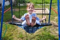 Happy little girl dressed in a blue striped dress is enjoying a swing ride on a sunny summer playground in the garden. Royalty Free Stock Photo