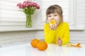 Happy little girl eating big tangerine whole while sitting at table Royalty Free Stock Photo