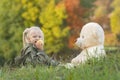 Happy little girl eats apple and plays with large teddy bear sitting on grass. Child on on autumn day in nature Royalty Free Stock Photo