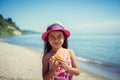 Happy little girl enjoying sunny day at the beach. Eats some hotdog