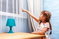 Happy little girl excited child pointing her finger at the window smliling kid shows points at something outside the window, night Royalty Free Stock Photo