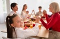 Happy little girl with family saying prayer before festive Thanksgiving or Christmas dinner, celebrating holiday at home