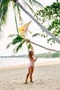 Happy little girl with flying kite on tropical beach under palm tree Royalty Free Stock Photo