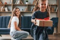 Happy little girl is with gift box. Young mother with her daughter is together at apartment Royalty Free Stock Photo