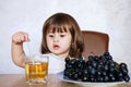 Happy little girl with glass of grapes juice. Positive toddler in front of a table with fresh fruit Royalty Free Stock Photo