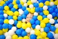 Happy little girl having fun in ball pit in kids indoor play center. Child playing with colorful balls in playground ball pool.