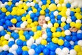 Happy little girl having fun in ball pit in kids indoor play center. Child playing with colorful balls in playground ball pool.