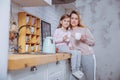 Happy little girl and her beautiful young mother have breakfast together in a white kitchen. They hug and drink tea. Maternal care Royalty Free Stock Photo