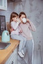 Happy little girl and her beautiful young mother have breakfast together in a white kitchen. They hug and drink tea. Maternal care Royalty Free Stock Photo