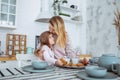 Happy little girl and her beautiful young mother have breakfast together in a white kitchen. Mom hugs and kisses daughter. Royalty Free Stock Photo