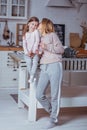 Happy little girl and her beautiful young mother have breakfast together in a white kitchen. Mom hugs and kisses daughter. Royalty Free Stock Photo