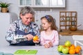 Happy little girl and her grandmother have breakfast together in a white kitchen. They are having fun and playing with fruits. Royalty Free Stock Photo