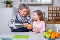 Happy little girl and her grandmother have breakfast together in a white kitchen. They are having fun and playing with fruits. Royalty Free Stock Photo