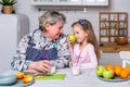 Happy little girl and her grandmother have breakfast together in a white kitchen. They are having fun and playing with fruits. Royalty Free Stock Photo