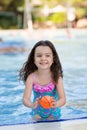 Happy little girl with her hair down in a bright swimsuit playing ball in the pool on a Sunny summer day Royalty Free Stock Photo
