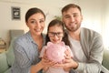 Happy little girl with her parents  holding piggy bank indoors. Money savings concept Royalty Free Stock Photo