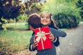 Happy little girl is holding gift in red box and smiling while hugging little boy Royalty Free Stock Photo