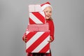 Happy little girl holding many Christmas gifts isolated gray background. The child looks out from behind a large pile of present Royalty Free Stock Photo