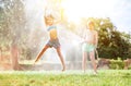 Happy little girl jumps under water, when brother pours her from garden hose. Hot summer days activity