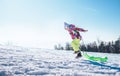 Happy little girl jumps up on the snow slope with bright plastic