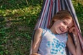 A happy little girl lies in a hammock in the garden in the summer. A child in a hammock during the holidays smiles in Royalty Free Stock Photo