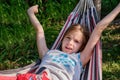 A happy little girl lies in a hammock in the garden in the summer. A child in a hammock during the holidays smiles in Royalty Free Stock Photo