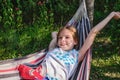 A happy little girl lies in a hammock in the garden in the summer. A child in a hammock during the holidays smiles in Royalty Free Stock Photo