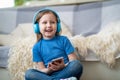 Happy little girl listening to music in blue headphones, at home Royalty Free Stock Photo