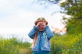 Happy little girl with long blonde hair in straw hat and yellow sunglasses walking on meadow and showing glasses fingers Royalty Free Stock Photo