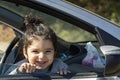 Happy little girl looking out the window of a car in outdoor area