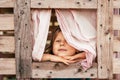 Happy little girl looks out window of wooden children& x27;s house. Holidays in village. Childhood. Royalty Free Stock Photo
