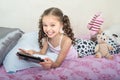 Happy little girl lying on bed with tablet computer
