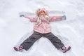 Happy little girl lying in the snow in the shape of an angel. Winter childrens vacation, top view