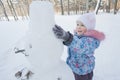 Happy little girl making winter snowman from snow