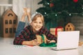 A happy little girl opens a gift under the Christmas tree at home and communicates with her grandparents via a laptop via video Royalty Free Stock Photo