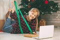 A happy little girl opens a gift under the Christmas tree at home and communicates with her grandparents via a laptop via video Royalty Free Stock Photo