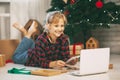 A happy little girl opens a gift under the Christmas tree at home and communicates with her grandparents via a laptop via video Royalty Free Stock Photo