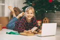 A happy little girl opens a gift under the Christmas tree at home and communicates with her grandparents via a laptop via video Royalty Free Stock Photo