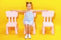 Happy little girl with outstretched arms sits on a chair against the background of a yellow wall. Royalty Free Stock Photo