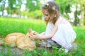 Happy little girl pets the cat in summer outdoors