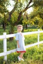 Happy little girl with pigtail around her head standing at white wooden fence on background garden. Copy space. Smiling girl stand Royalty Free Stock Photo