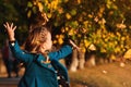 Happy little girl playing with autumn leaves. Cute child having fun in park. Stylish baby girl in blue coat throws autumn leaves o