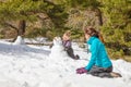 Happy little girl playing with snowman next to woman