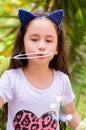 Happy little girl playing with soap bubbles on a summer nature, wearing a blue ears tiger accessories over her head in a Royalty Free Stock Photo