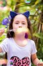 Happy little girl playing with soap bubbles on a summer nature, wearing a blue ears tiger accessories over her head in a Royalty Free Stock Photo