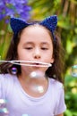 Happy little girl playing with soap bubbles on a summer nature, wearing a blue ears tiger accessories over her head in a Royalty Free Stock Photo